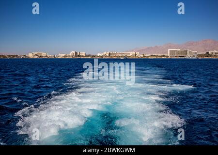 Gulf of Aqaba as seen from tourist boats, Jordan. Some front line hotels and the crystal blue water of Red Sea, sunny winter afternoon, water foam from the speeding vessel Stock Photo