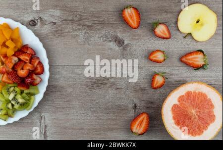 fruit salad and fresh strawberries on wooden table. healthy and dietary breakfast, food preparation concept.  Stock Photo