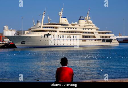 Man standing at the Corniche looking at the Sultan Qaboos luxury yacht Al Said moored in Mutrah Harbour, Muscat, Sultanate of Oman Stock Photo