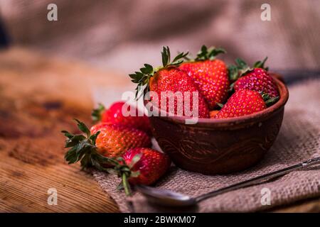 Fresh strawberries in a bowl on wooden table with low key scene. Stock Photo