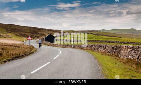 Teesdale, England, UK - May 25, 2011: A touring cyclist rides on a country road through the moorland hills of the North Pennines in County Durham Stock Photo