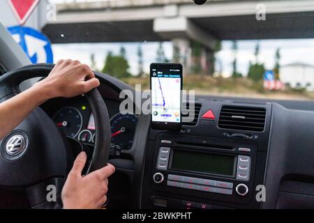 Driving and using waze maps application on smartphone on car dashboard, Driver using maps app for showing the right route through the traffic of city. Stock Photo