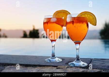 two glasses with Spritz Veneziano, an Italian cocktail drink from aperol, prosecco and soda on a wall at the water against a clear sunset sky, copy sp Stock Photo