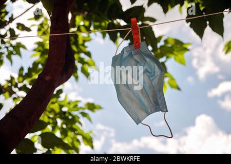 Disposable medical mask hanging on pegged clothesline for reused. tree in the background Stock Photo