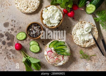 Crispbread sandwiches with ricotta, radish and fresh cucumber on a light kitchen stone or slate countertop. Top view flat lay background. Stock Photo