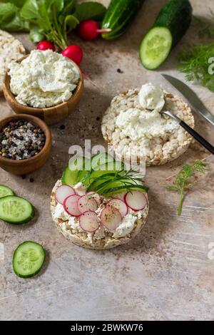Crispbread sandwiches with ricotta, radish and fresh cucumber on a light kitchen stone or slate countertop. Copy space. Stock Photo