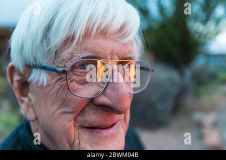 Close up of senior man smiling, and flames reflected in his glasses Stock Photo