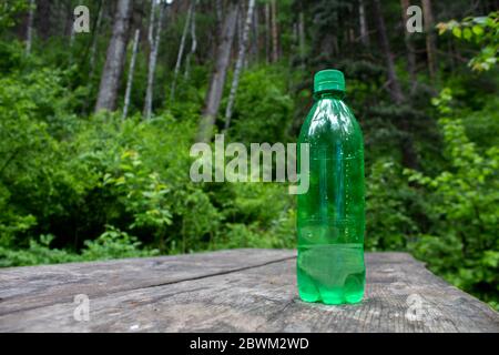 Green almost empty plastic bottle on a wooden table in the forest Stock Photo
