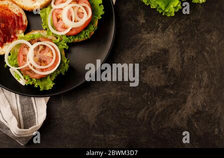 Raw minced beef, fresh bun, slice of cheese, tomato, onion rings, pickle, lettuce, herbs. Homemade hamburger ingredients. Black board background. Spac Stock Photo
