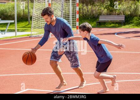 Father and son playing basketball barefoot on a playground Stock Photo