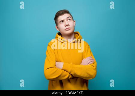 the guy in a sweatshirt folded his arms over his chest and looks up thoughtfully Stock Photo