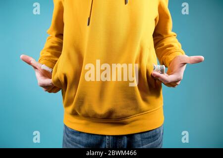teenager shows a syringe with a drug and money, taking it out of the pockets of a sweatshirt on a blue background. Without a face, close-up Stock Photo