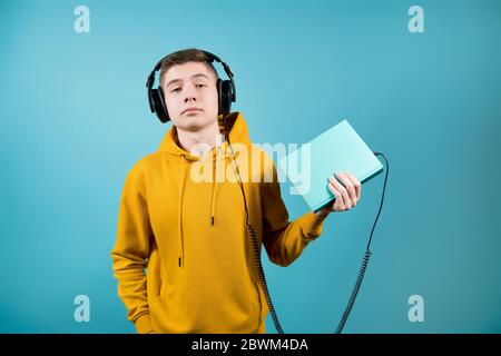 a teenager holds a book into which the plug from the headphones is stuck Stock Photo