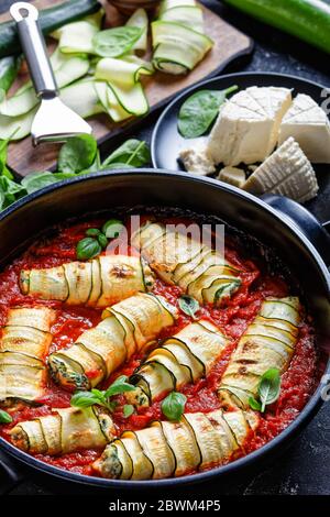 Keto diet dish recipe of rolled zucchini strips with a filling of ricotta mixed with baby spinach, fresh basil leave baked in tomato sauce served on a Stock Photo