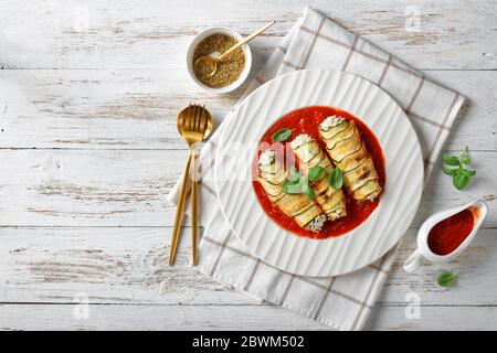 Italian appetizer: zucchini rollatini filled with ricotta, garlic and spinach baked in tomato sauce, served on a white plate with basil on top on a wh Stock Photo