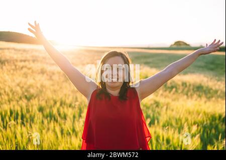 Young woman arms raised up to sky, celebrating freedom. Positive emotions feeling life perception success, peace of mind concept. Free Happy girl in summer meadow enjoying sunset in nature .