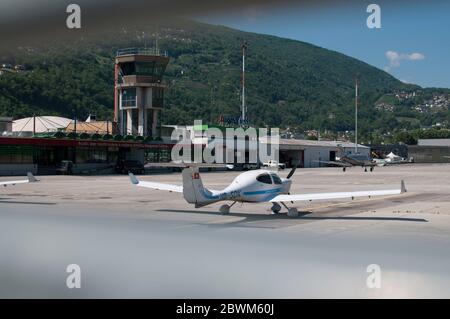 Agno, Ticino, Switzerland - 21st May 2020 : View through the gate of the Lugano-Agno airport in Switzerland with a small airplane parked in front of i Stock Photo