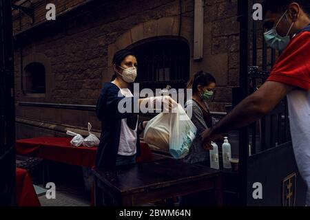 Barcelona, Spain. 2nd June, 2020. A volunteer wearing a protective face mask hands out free food rations for the economically struggling in Barcelona's Santa Anna Church during the second phase of a gradual way to 'the new normal' rolling back a nearly seven weeks long nationwide strict lockdown due to the spread of the corona virus. Spain's economy contracted by 5.2% in the first quarter and the GDP is expected to shrink up to 13% this year due to the coronavirus crisis raising the unemployment rate to about 19%. Credit: Matthias Oesterle/Alamy Live News Stock Photo