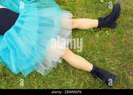 Woman in big black boots and a blue skirt lies on green grass. After party concept Stock Photo