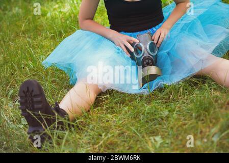 Woman in blue skirt with gas mask sits on green grass. Environmental protection, biohazard and ecological concept Stock Photo