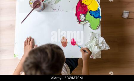 High angle view of young boy painting on paper with colorful paints.