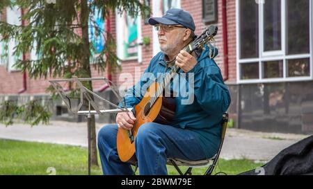 02/06/2020: A street musician plays guitar music for people passing by. An elderly man with a guitar on the street plays popular music for the public. Stock Photo