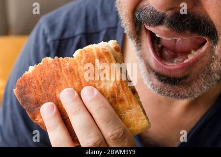 Mustachioed man holds bread and is ready to bite bread. Man opens mouth to eat bread. Stock Photo