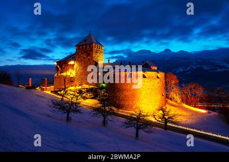 Vaduz, Liechtenstein. Illuminated castle of Vaduz, Liechtenstein at sunset - popular landmark at night, with sunset sky, mountains at the background Stock Photo