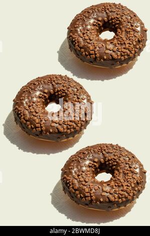 Three chocolate donats with sunny shadows on vertical background. Fresh delicious desserts. Creative food pattern, top view. Geometrical trendy Stock Photo