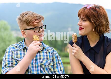 A young red-haired woman and a boy eating ice cream in a city on a hilly background.Young friends eat ice cream in a park. Stock Photo