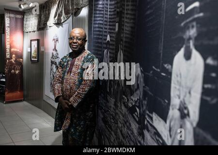 The director of the national museum in Benin city infront of a photograph depicting British in the royal palace surrounded by looted Benin Bronzes Stock Photo