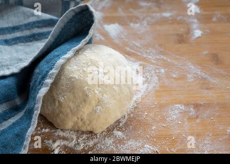 yeast dough for bread or cake will be covered with a kitchen towel to rest and rise on a wooden baking board, copy space, selected focus, narrow depth Stock Photo