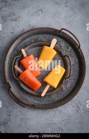 Papaya and mango popsicle on round metal tray on grey background, top view Stock Photo