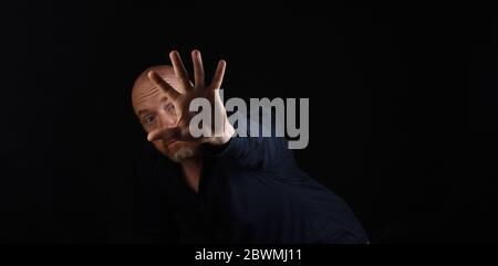 dark portrait of a man with hand outstretched stop sign on black bakcground Stock Photo