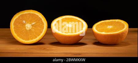 oranges on a wooden table, chopped oranges, three halves of oranges Stock Photo