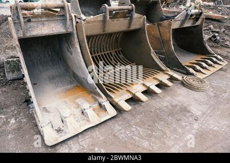 Large used excavator shovels stand side by side on a cement floor. Stock Photo