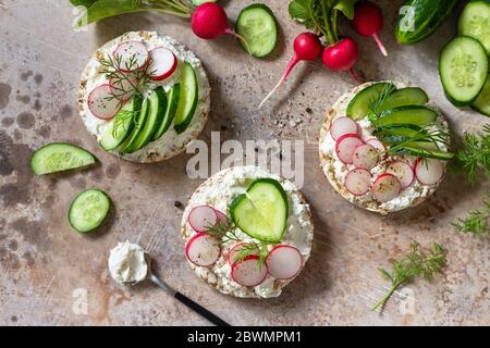 Crispbread sandwiches with ricotta, radish and fresh cucumber on a light kitchen stone or slate countertop. Top view flat lay background. Stock Photo