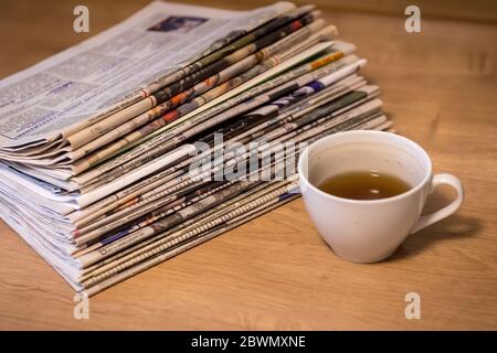 selective focus of the drunk cup of tea stacking newspapers folded place on wooden table Stock Photo