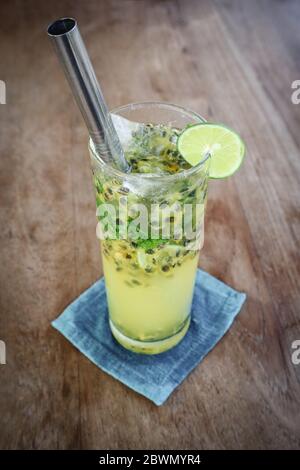 Passion fruit mojito cocktail with metal drinking straw on wooden table in cafe. Stock Photo