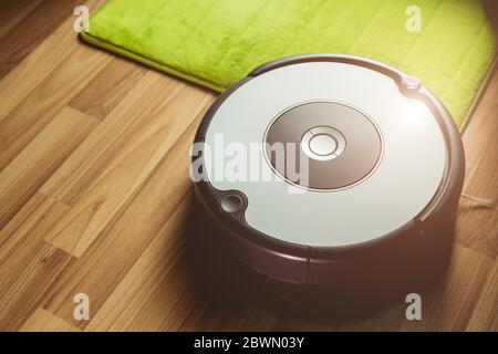 Robot vacuum cleaner cleaning on wooden floor with carpet on the apartment home ground sunny light. Stock Photo