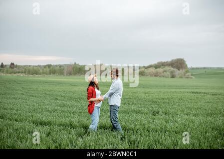 Portrait of a pregnant woman with her boyfriend dressed casually with hats standing together on the greenfield. Happy couple expecting a baby, young family concept Stock Photo