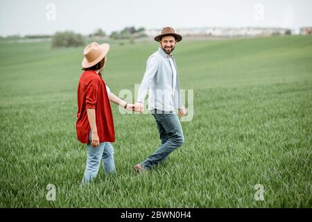 Pregnant woman with her man having fun together, walking on the greenfield. Happy couple expecting a baby, young family concept Stock Photo