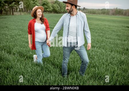 Pregnant woman with her man having fun together, walking on the greenfield. Happy couple expecting a baby, young family concept Stock Photo