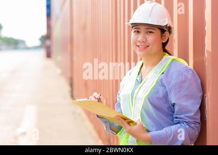 Asian young teen happy worker checking stock in shipping port work manage import export cargo containers. Stock Photo