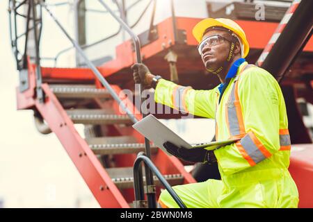 Black African Staff foreman intend to work loading worker using laptop computer to control cargo shipping in logistic warehouse. Stock Photo