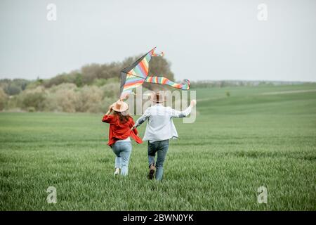 Happy couple having fun together, playing with kite on the greenfield. Happy couple expecting a baby and young family concept Stock Photo