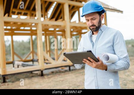 Architect or builder using digital touchpad on the construction site outdoors. Concept of building and designing wooden frame house Stock Photo