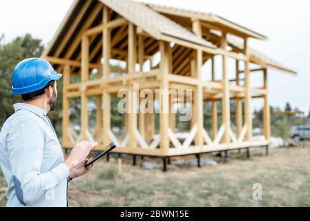 Architect or builder with digital touchpad near the wooden house structure, building and designing wooden frame house Stock Photo