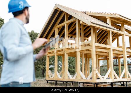 Architect or builder with digital touchpad near the wooden house structure, building and designing wooden frame house. Image focused on the house Stock Photo