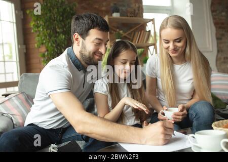 Mother, father and daughter at home having fun, comfort and cozy concept. Looks happy, cheerful and joyful. Beautiful caucasian family. Spending time together, drinking tea, playing games. Stock Photo